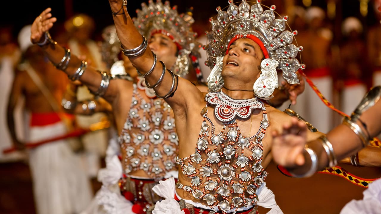 Kandyan dancers in silver ves headdresses and white costume, performing.