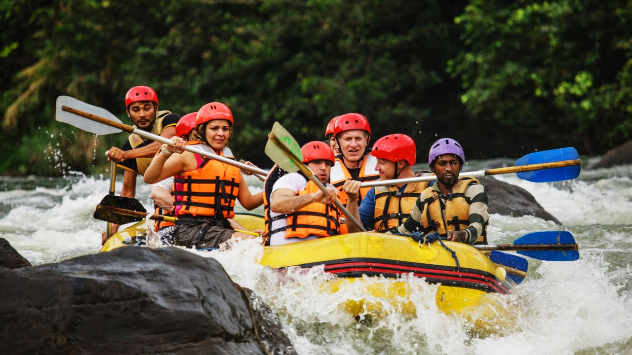 A raft of paddlers in helmets and life jackets coming through white water on the Kelani at Kitulgala.