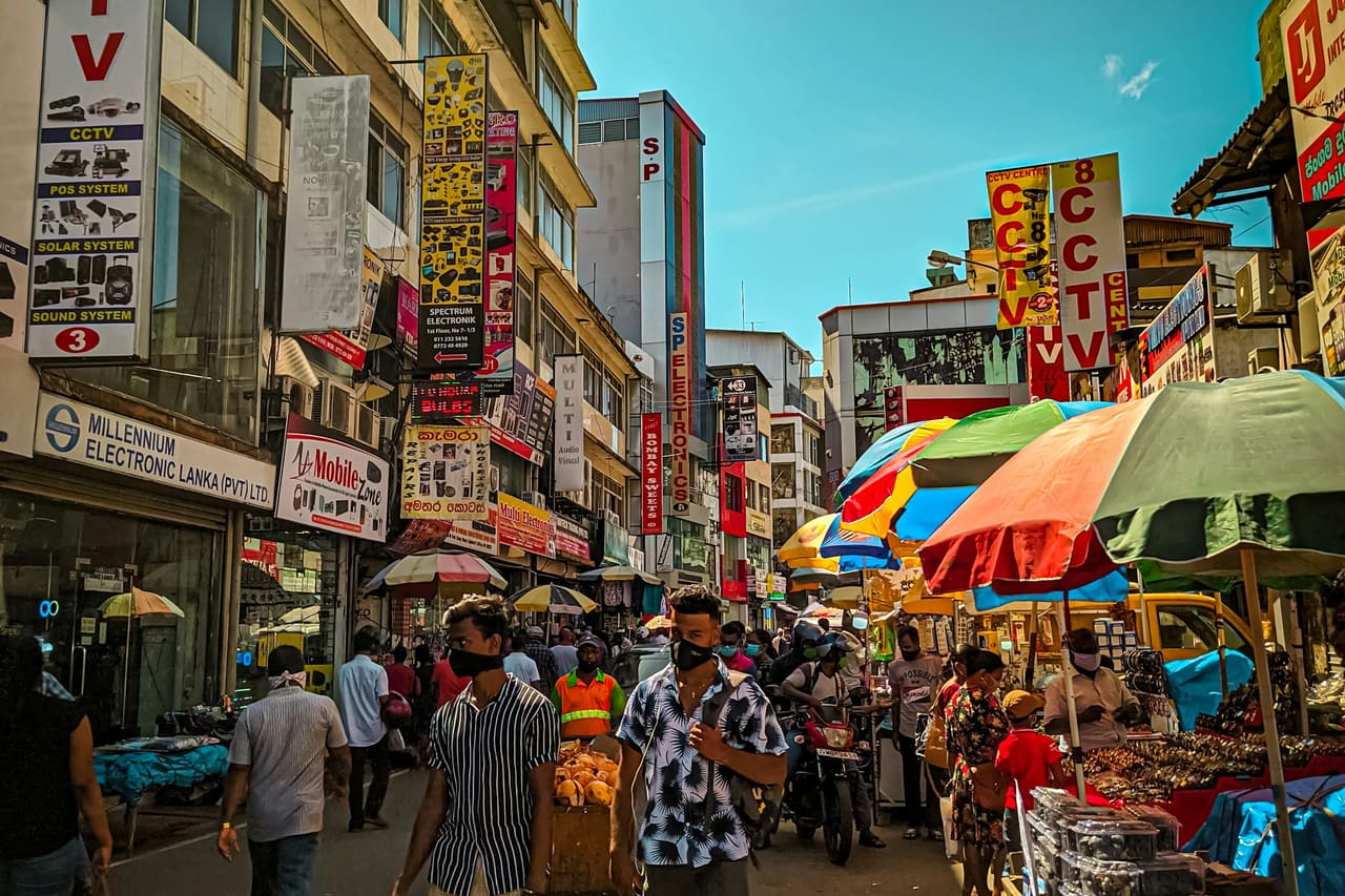 A busy Pettah street in Colombo, shopfronts and market umbrellas along both sides.