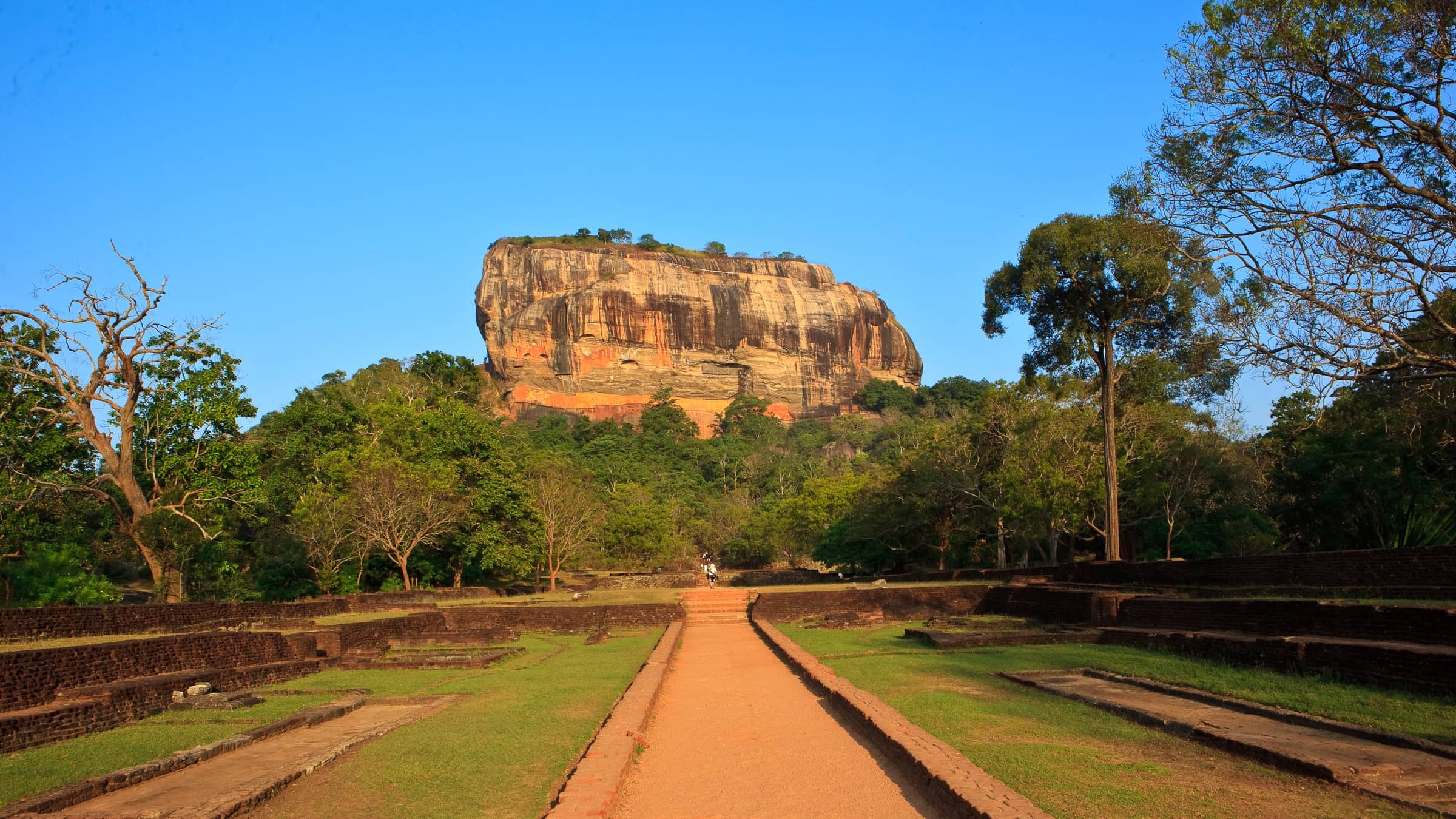 Sigiriya rock seen from the causeway through the water gardens, under a clear blue sky.