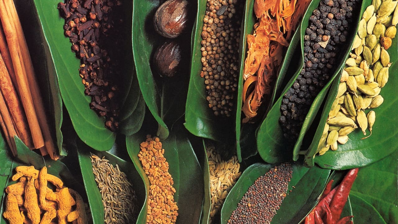 Cinnamon quills, cardamom pods, peppercorns and nutmeg laid out on banana leaf.