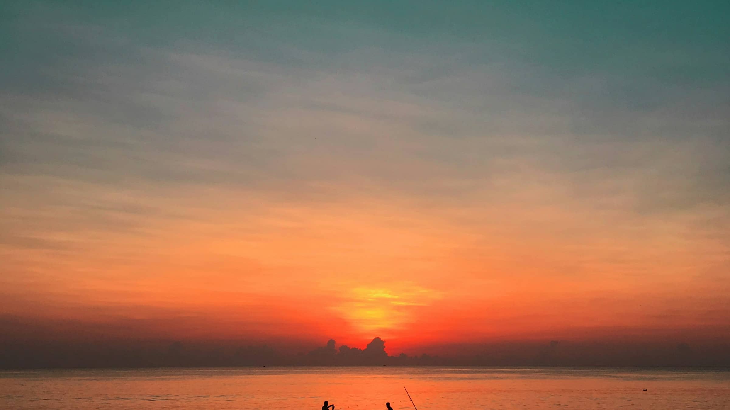 An outrigger canoe silhouetted on an orange sea at sunset.