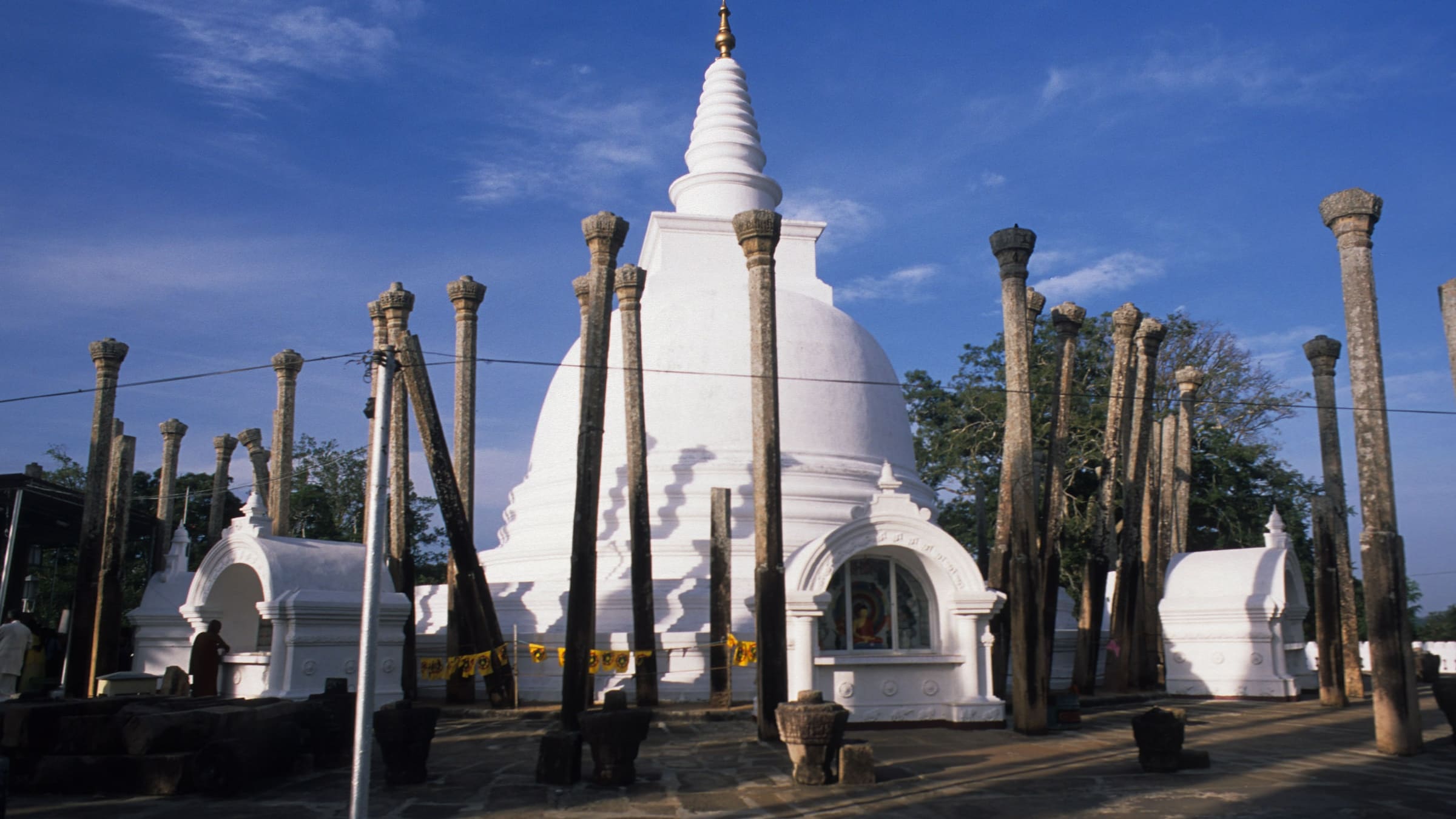 The white Thuparamaya dagoba at Anuradhapura, ringed by slender stone pillars under a blue sky.